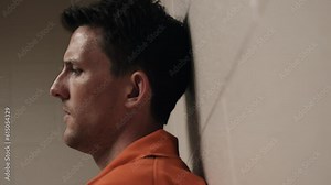 An unhappy man, sad, depressed attractive, handsome man, criminal prisoner, inmate in orange jumpsuit sitting in prison cell.