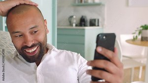 Video call, phone and smartphone man with virtual technology in living room. African american male sitting at home on the sofa talking to online internet contact, smiling and laugh on social media