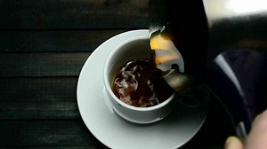 Download pouring coffee from a coffee pot into a cup on a wooden background for free