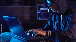 Hacker typing program code while committing a cybercrime hacking a system firewall in the dark under neon light