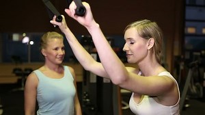 Female fitness trainer helping woman on lat machine in gym