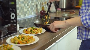 woman cook puts fried vegetables and poultry meat on plates from a frying pan. Cooking juicy pieces of meat and fresh vegetables. She gives each member of the family a portion. Healthy home cooking