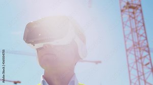 Professional builder in VR helmet standing in front of construction site and using virtual and augmented reality technologies. Office building and crane background. Real estate and investment.