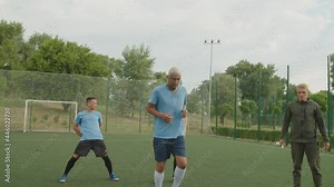 Team of diverse mixed race soccer players in football uniform jumping barriers and performing dribbling exercise outdoors, improving slalom skills on football pitch at dawn, controlled by young coach