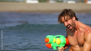 Young attractive man having fun in water playing with water guns. Friends on vacation. Fun, togetherness, holiday, lifestyle concept.