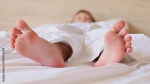 Little girl's feet stick out from under a white blanket at the morning.