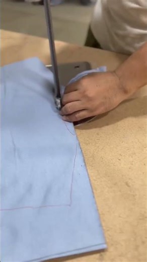 skilled tailor or seamstress using an industrial sewing machine to stitch light blue fabric