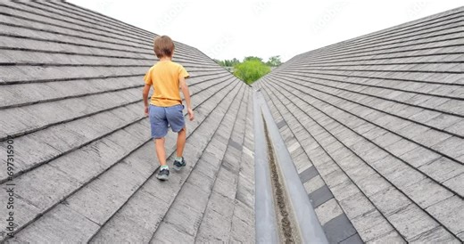 Young boy looks back over his shoulder, capturing final glimpse of camera. Fearless young boy defying boundaries as he ventures along rooftop's inclined path