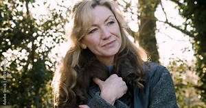 Attractive happy thoughtful smiling middle aged woman in her forties or fifties outside in golden hour evening sunshine Stock Video