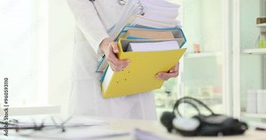 Woman doctor carries stack of ring binders putting on table in hospital. Female medic in uniform prepares for boring paperwork slow motion