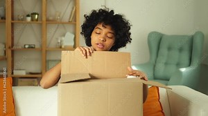 African girl unpacking delivery looking in box. Happy woman opening carton box. Female getting parcel looking at delivered goods items. Satisfied client positive feedback quick express deliver