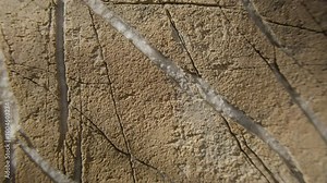 A detailed close-up of a cracked rock surface displaying distinct linear patterns. The natural cracks create intricate geometric shapes, highlighting the texture of the weathered stone.
