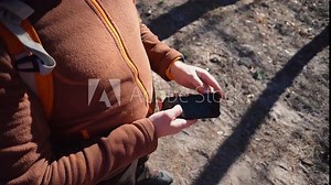 theme tourism and technology. Young caucasian man with beard and backpack. Hiking tourist in pine forest uses technology, hand holding mobile phone to touch the screen. Gps application orientation