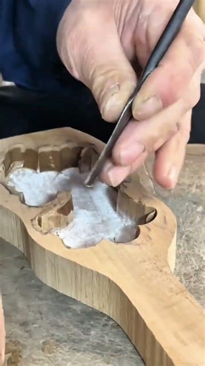 carving a detailed wooden mold using a sharp metal chisel tool on a textured surface in a workshop