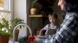 Free stock video - Side view of caucasian woman washing vegetables and fruits in the sink. her son helps to her