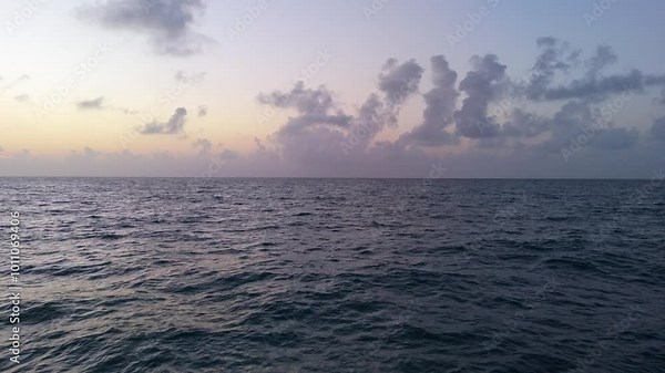 A slow-motion drone captures the sea at sunrise with blue and orange hues. Clouds on the horizon, waves rolling. The camera films the water from different perspectives.