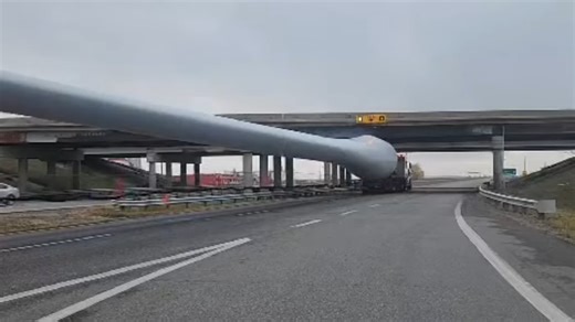 Oversized truck hauls a wind turbine blade under a low bridge