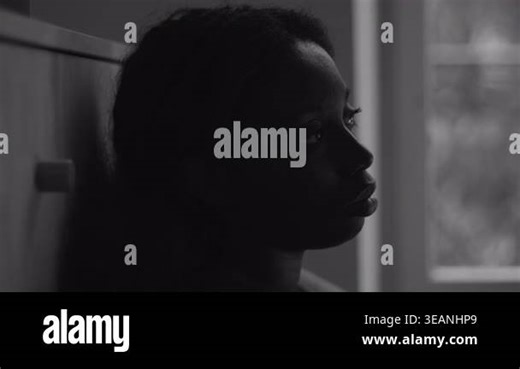African American woman in monochrome profile with blank expression near window suggesting deep despair mental illness isolation and loss of emotional connection Stock Video Footage - Alamy