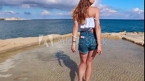 Beautiful girl walking in the water and looking at the panorama of the sea / Valletta, Malta island