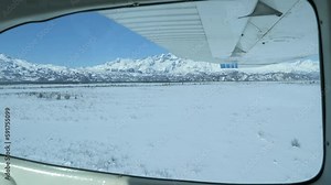 Flight over the icy waters Cook Inlet in Alaska during winter with vast expanses of snow-covered forests, rivers, valleys, and mountain peaks of the Chugach Mountain Range.