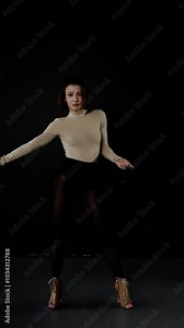Young woman in a beige leotard and black tights performs a contemporary dance routine on a minimalist stage featuring a solid black backdrop