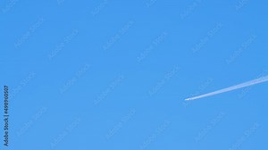 A plane flies high in the sky and leaves a white trail. Summer time lapse, blue sky. Video, screensaver background, for titles, intro, transition. UHD 4K.