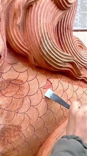 carefully carving fish scales on wooden sculpture with sharp steel chisel tool to create patterns