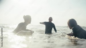 Three surfer guys in wetsuits talking while in the water in the sea with their surfboards in the summer. Communication and learning how to surf
