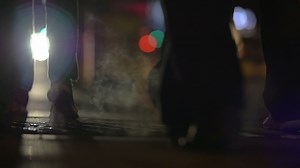 People walking over steaming manhole at night