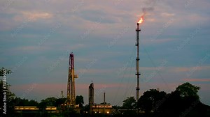Fire burning on top of gas flare stack chimney on petroleum refinery against sunset red sky