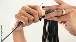 Close up of the hands of a female hairstylist doing a perm rolling the clients hair onto fine rollers or curlers for a curly or wavy effect