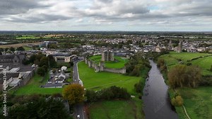 Trim Castle, County Meath, Ireland, October 2023. Drone panoramic clockwise orbit above town and grassy field with historic Medieval Fortress centered under overcast sky.