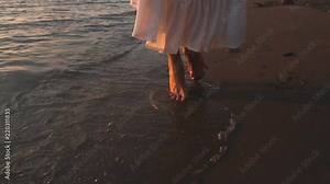 Beautiful bare feet on the beach. Sea foam washes female legs. Image of feet in the sand on the shore in the wave.