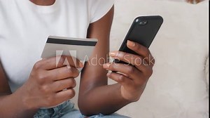 Close-up young African American female shopper holding smartphone and credit card in hands using instant easy mobile payments making purchase in online store receiving cashback. E-banking service