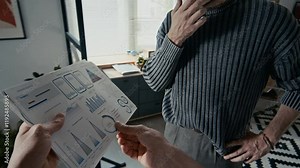 POV of man holding printed charts and graphs and discussing project questions with his male colleague, standing in modern open space office