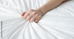 Woman's hand squeezing sheet on the bed, close-up, slow motion. Hand grabs a white crumpled blanket