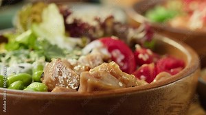 Eating poke bowl close-up, taking meat with chopsticks. Traditional Hawaiian dishes made of sliced vegetables, fried meat food and greenery. Healthy food. Asian raw meal.