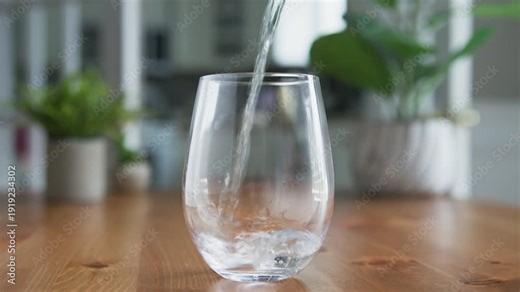 Pure fresh drinking water poured slowly from glass jug into transparent glass in macro close-up. Gentle stream fills the glass, bubbles rise, symbolizing hydration and thirst quenching in 4K