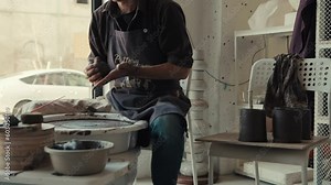 The potter works on the potter's wheel by the window. The process of making ceramic dishes from black clay.