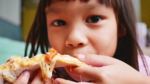 Download Cute little girls eating pizza. Hungry child taking a bite from pizza on a pizza party at home. Family vacation concept. for free