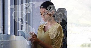 Woman by office window tapping and scrolling tablet, global map zooming reviewing technology data