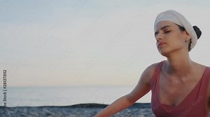 Young indian woman practice kundalini yoga in lotus pose, on the beach at sunset. Eyes close, turban on head, she makes a circular motion with her back. Sunrise background.