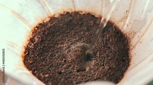 Filter V60 coffee. Hot water spilling fine jet in paper filter with ground coffee for brewing. Slow motion. Macro close-up.