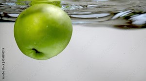 Two fresh green apples dropped into a bowl of water, underwater shot