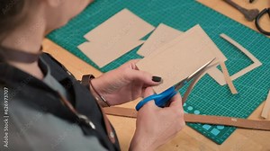 Over the shoulder high angle shot of specielist making cardboard patterns when making leather bag for client in workshop