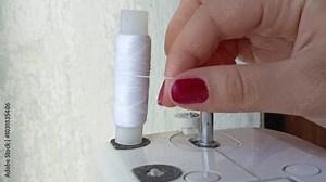 A woman inserts a spool of white thread into a sewing machine. Slow-motion video. Atelier. Seamstress at work. Advertising background. Sewing process.