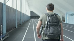 Following shot of professional male athlete with amputated leg walking in indoor stadium, sitting on bench and preparing to put on prosthetic runner blade