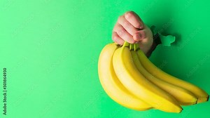 A woman holds a banana in her hand, inserted through a hole in torn green paper, 4k video
