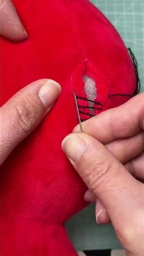 sewing a torn red plush fabric using a needle and thread to repair a soft toy in a workshop area