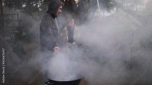 Single father fanning smoke while preparing backyard barbecue outdoors, cloudy smoke fills area. Part of series
